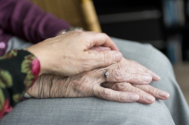 A woman covering an older woman's hands with her hand.