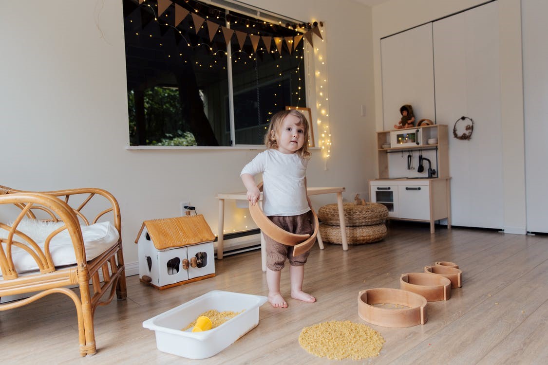 A little girl playing with pasta on wooden floors.