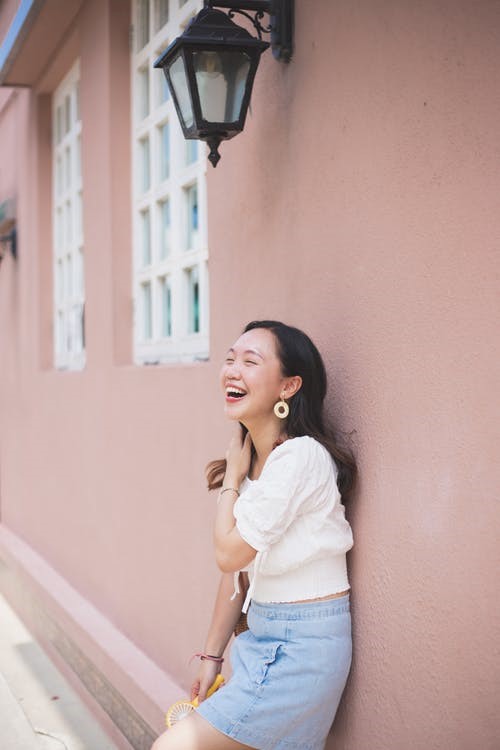 A woman standing against a pink wall with white windows.