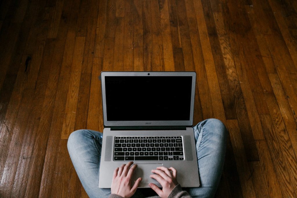 person sitting on a wooden floor and using a laptop