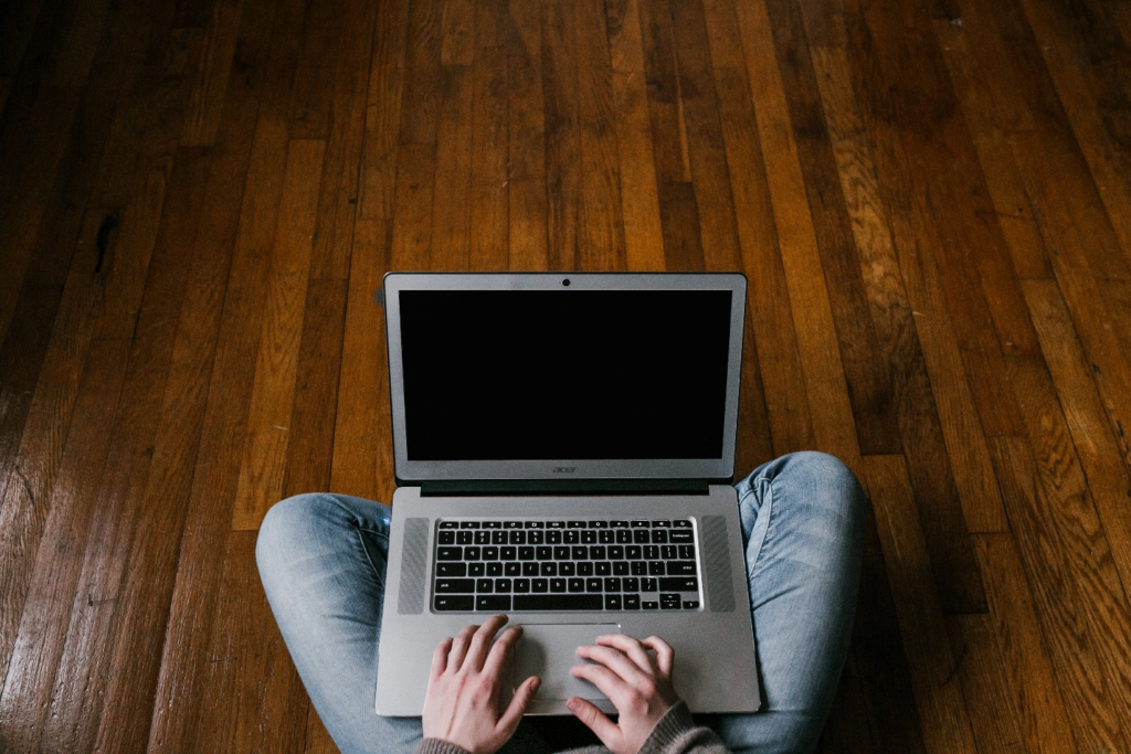 A person sitting on a hardwood floor using a Macbook