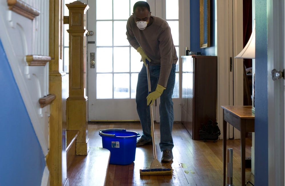 A masked man cleaning a wooden floor