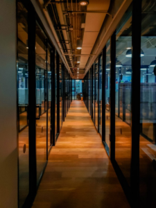 Hallway with gleaming wooden floors between glass partitions.