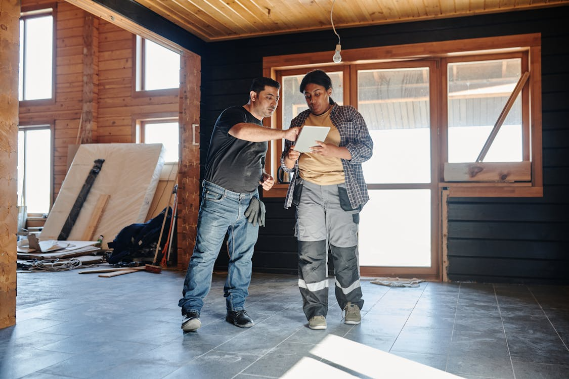 2 workers can be seen discussing over a paper in an under-construction wooden home